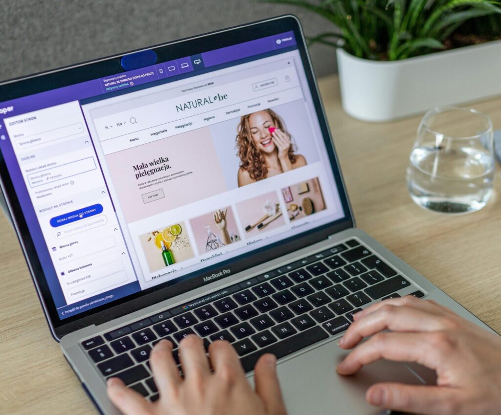Hands typing on a laptop showing an e-commerce website in a modern office setting.