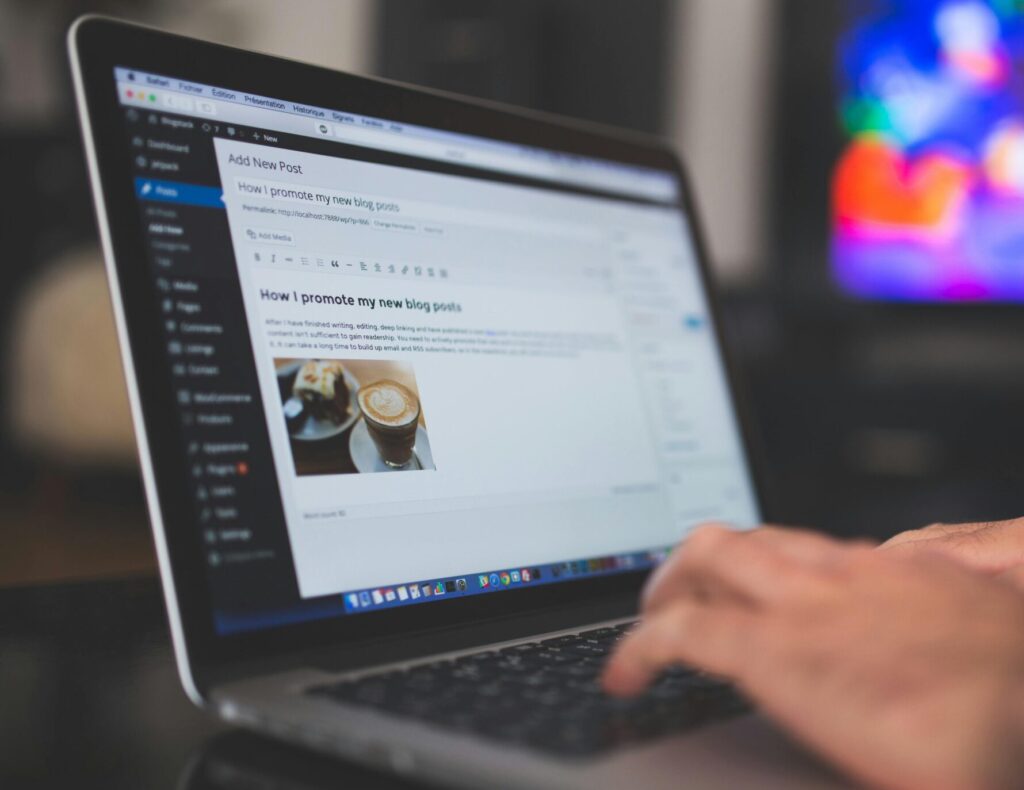 Hands typing on a laptop with a blog post visible, cozy indoor setting with colorful screen in background.